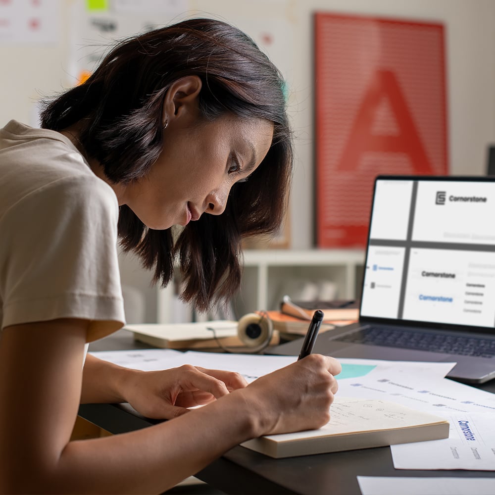 A user experience designer sketches concepts in a notebook, with a digital wireframe on her laptop, representing the agency's thoughtful and strategic design process.